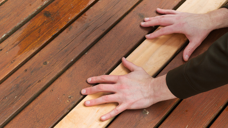 hands on a wood deck over a replaced board