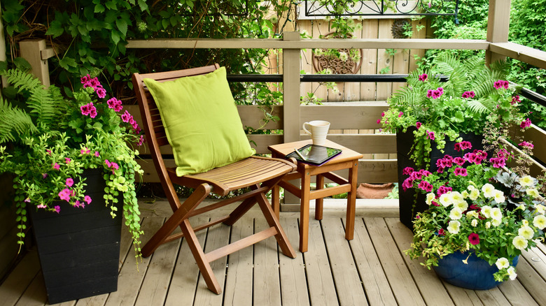 A wood deck surrounded by greenery with wooden furniture and colorful potted flowers