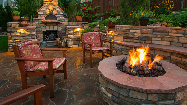 A backyard at dusk, with a fireplace in the background and a lit fire pit in the foreground