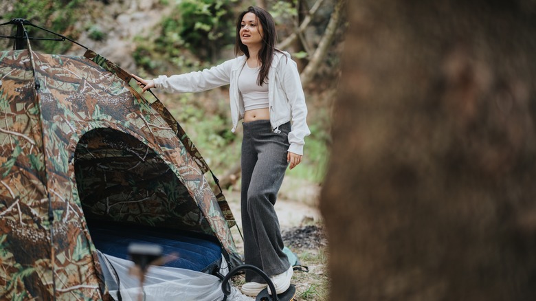 A woman in the woods standing next to a camouflaged tent