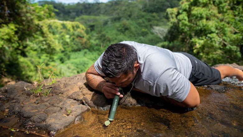 A man using a Lifestraw to drink from a natural water source