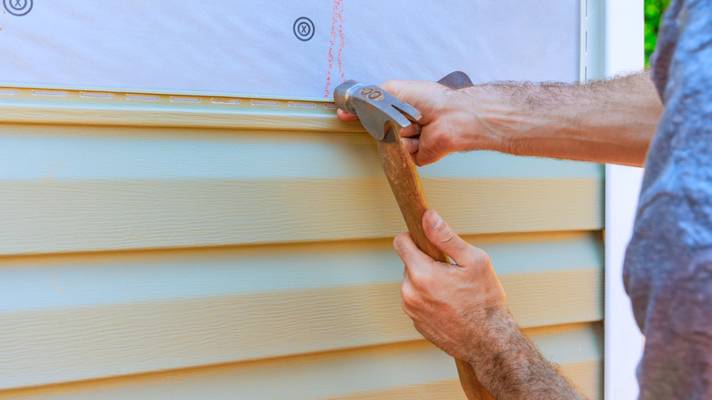 Worker replacing vinyl siding with a hammer