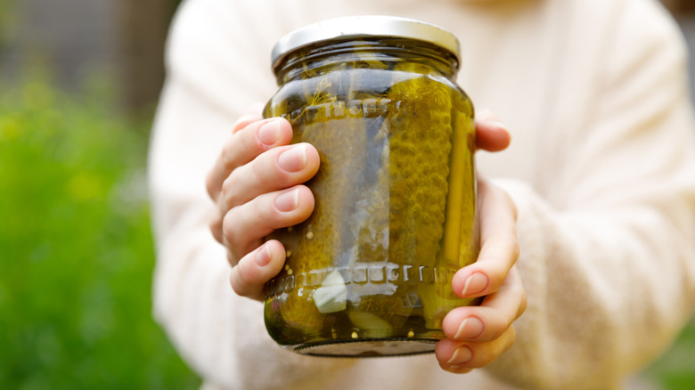 Woman holding a jar filled with dill pickles outside