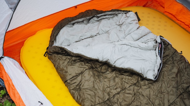 A wrinkled brown sleeping bag on a foam mat in an orange tent.