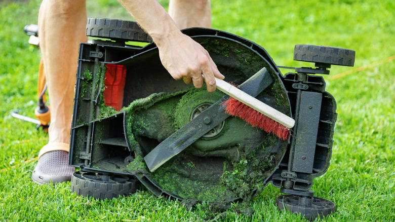 A homeowner cleans the debris from under their lawn mower
