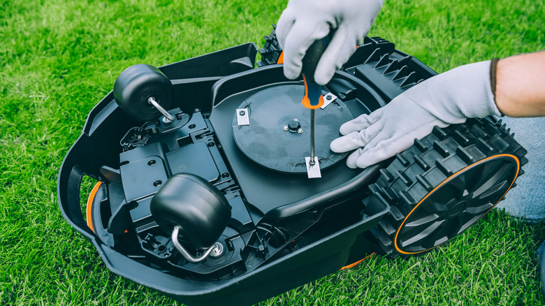 A homeowner uses a screwdriver to open up a small autonomous lawn mower