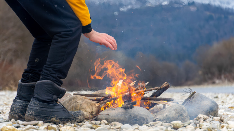 Person leaning over stone-lined campfire in winter