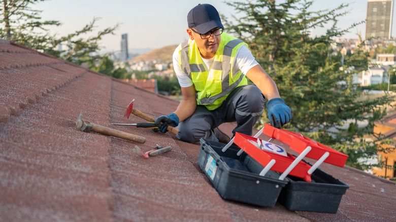 Worker with tool box on a shingled roof