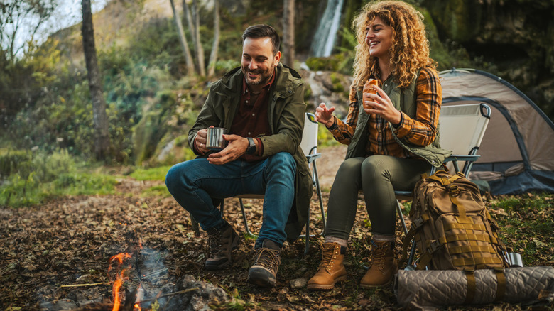 A young couple sits by the fire while camping