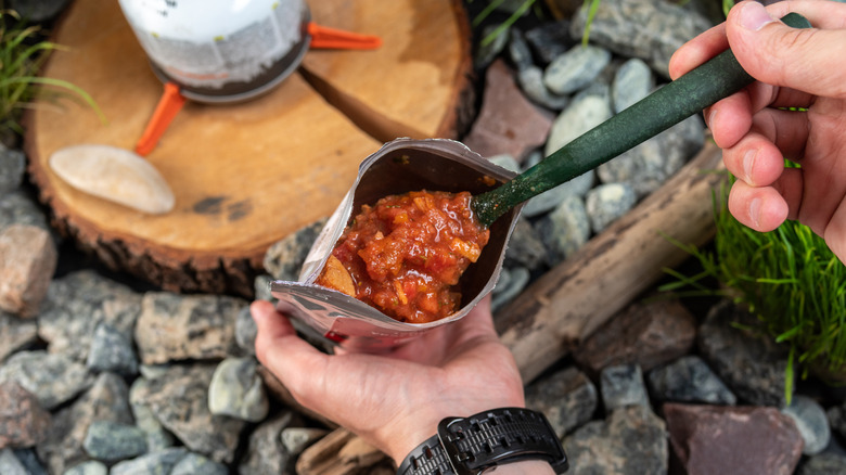Camper eating a reconstituted hot meal by a fire
