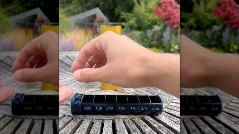 Hand hovering over pill organizer outside