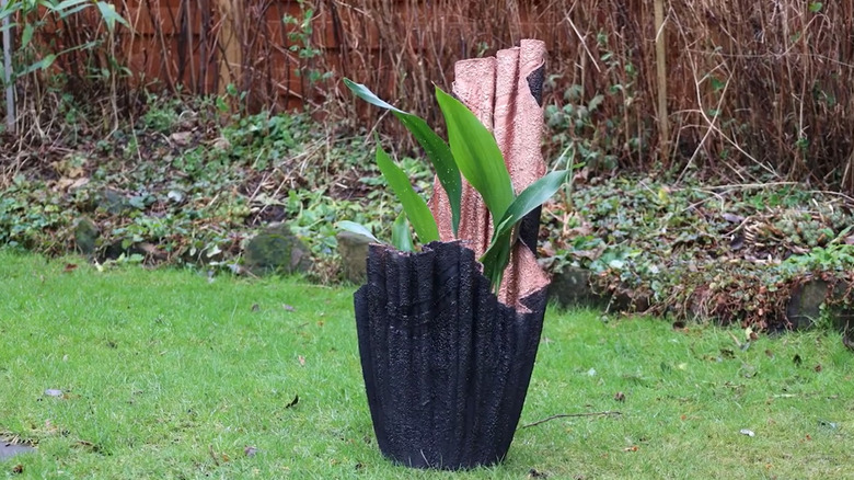 a planter made from a spray-painted and hardened towel holds a plant inside while sitting on lawn