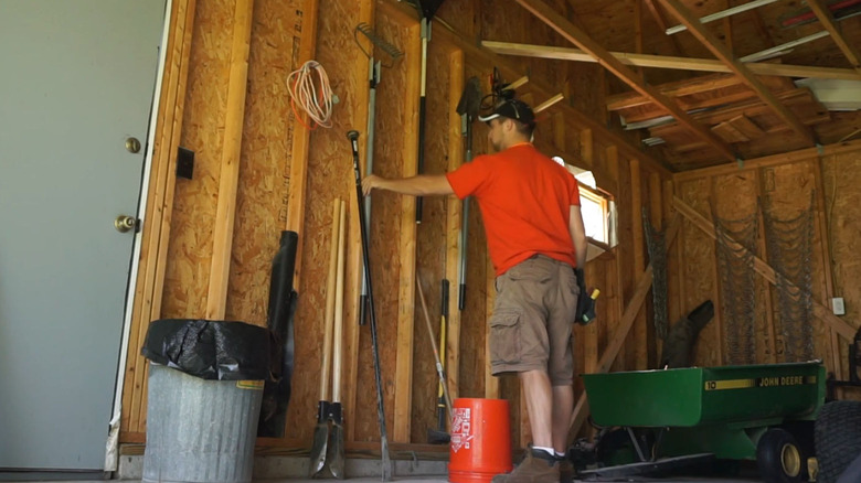 Someone putting their long-handle tools into DIY PVC holders in the garage.