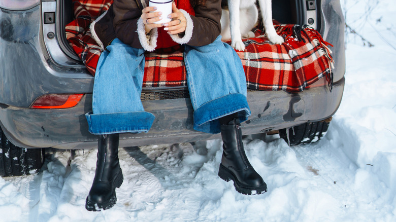 Woman and her dog sit in the back of an open tailgate on a vehicle