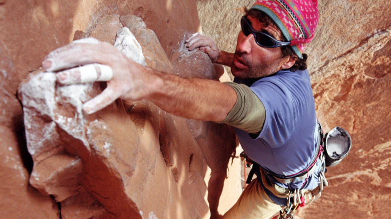 Man extending for handhold while rock climbing