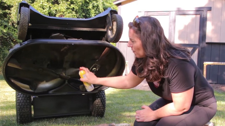 Woman spraying Pam on underside of lawn mower