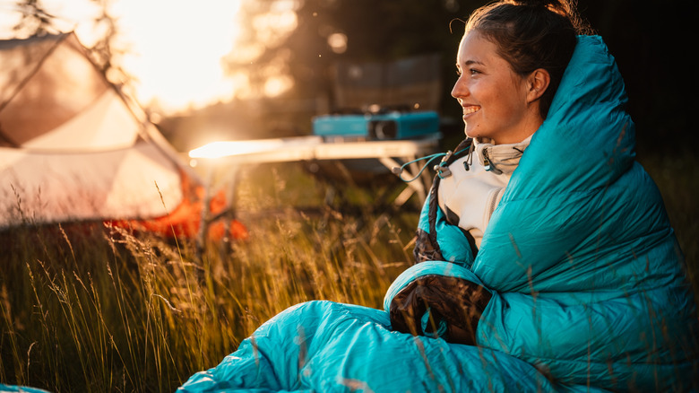 Woman sits up, smiling, in a sleeping bag