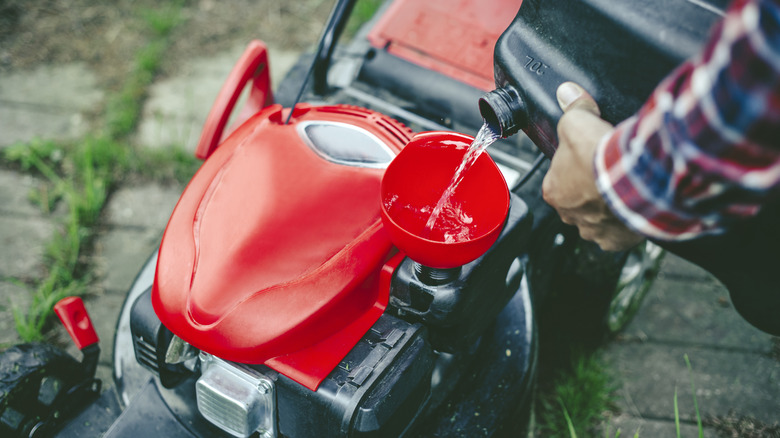 A man in a plaid shirt filling a red lawn mower with gas.