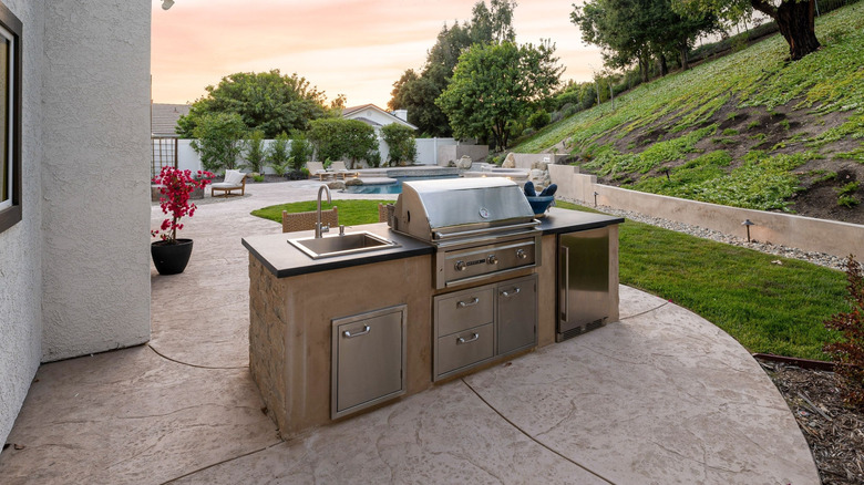 An outdoor kitchen island with stainless steel drawers, grill, and cupboards