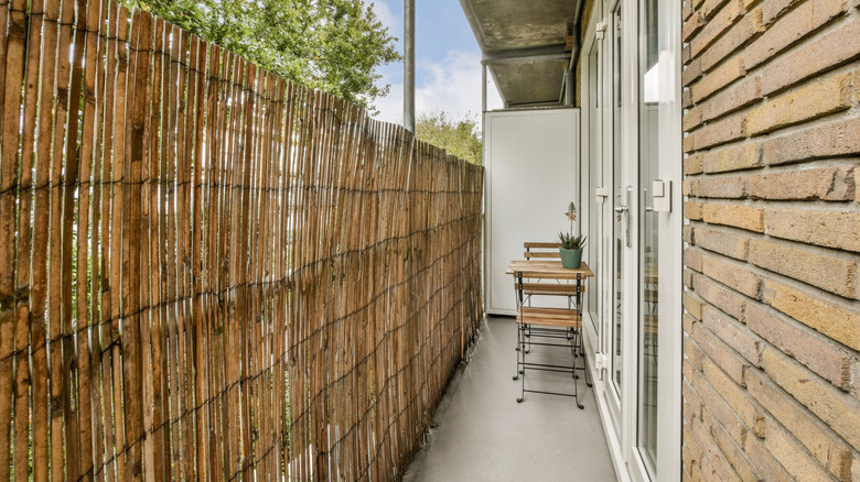 A narrow shared balcony screened by bamboo fencing