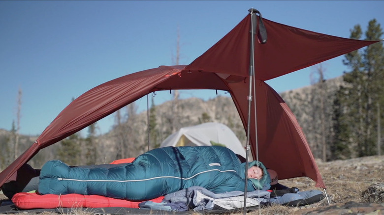 Women sleeping under a red open tent in a green Sidewinder sleeping bag.