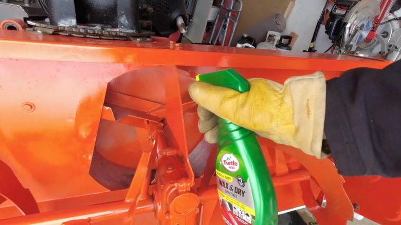 Person spraying Turtle Wax on parts of a snow blower