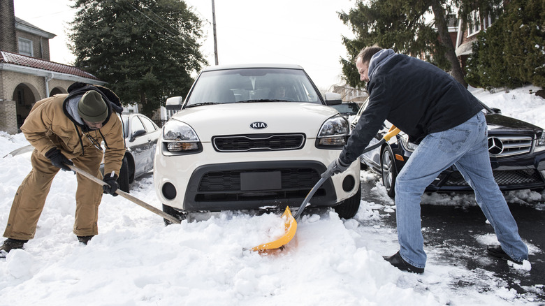neighbors shoveling snow to get a car unblocked