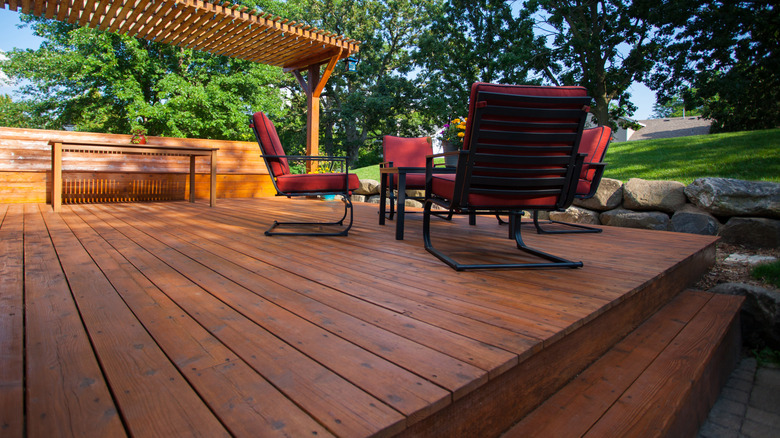 A stained deck outfitted with a pergola, red chairs, and tables