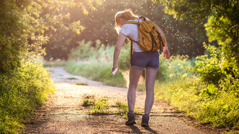 Woman spraying legs with insect repellent