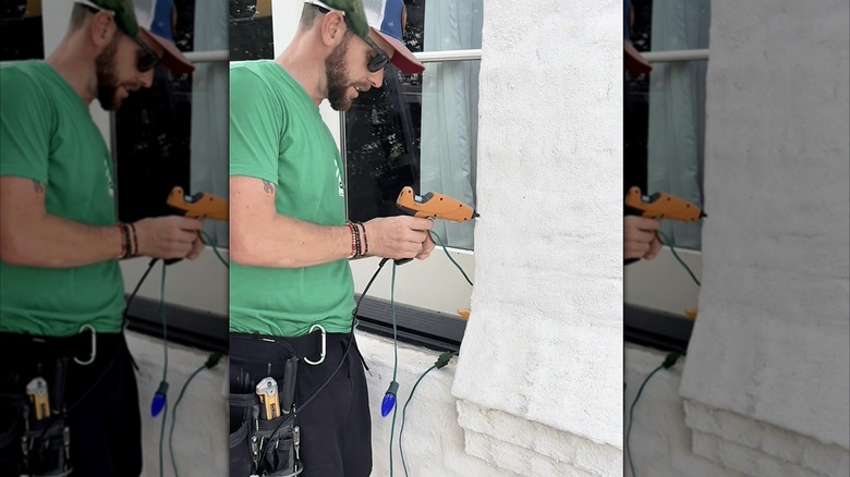 Person demonstrating hanging Christmas lights using hot glue