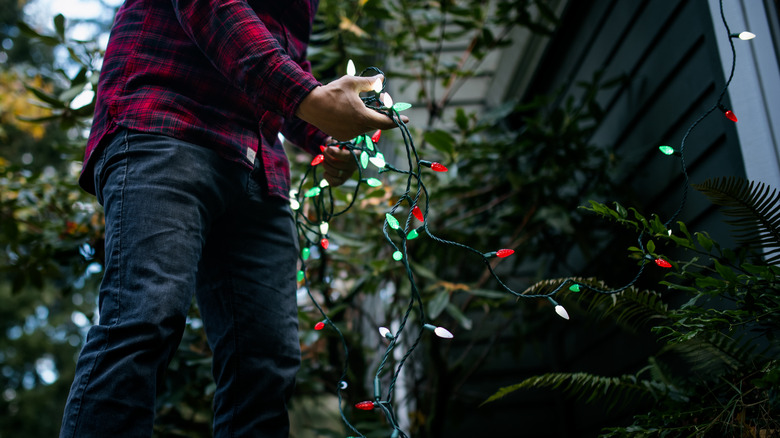 Man outside holds strand of Christmas lights