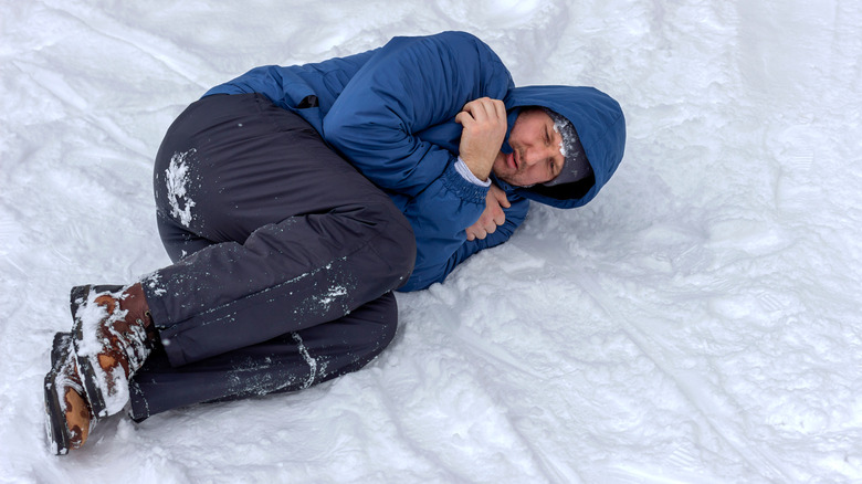 A man laying down, shivering in the snow