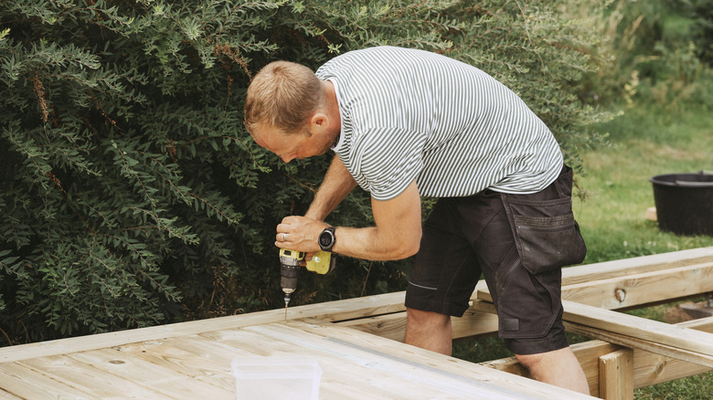 Man building a deck and using a drill to screw in the screws