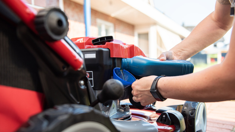 Person pouring oil in mower