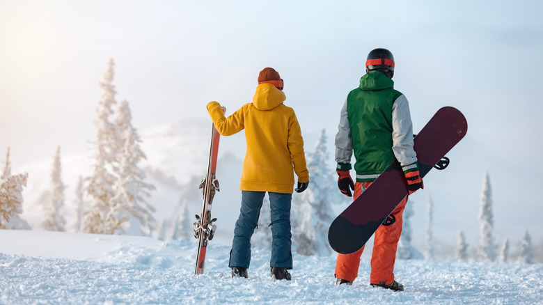 A skier and a snowboarder stop at a level area in the snow to check the view