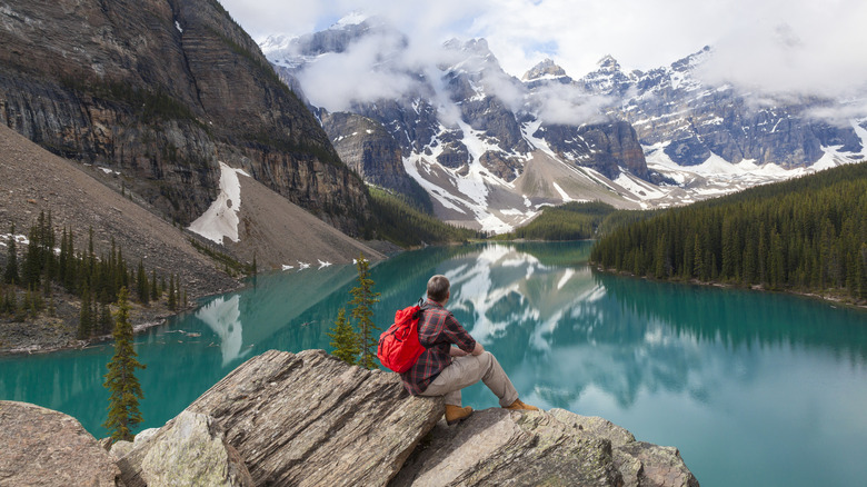 A man with a red backpack gazing out over Moraine Lake, Canada