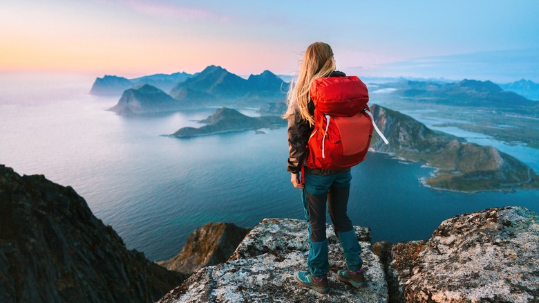 A woman with a red rucksack enjoying a view high over water