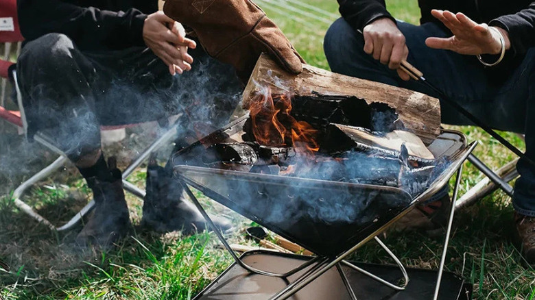 A fire burning in a Snow Peak Fire and Grill, with campers warming themselves