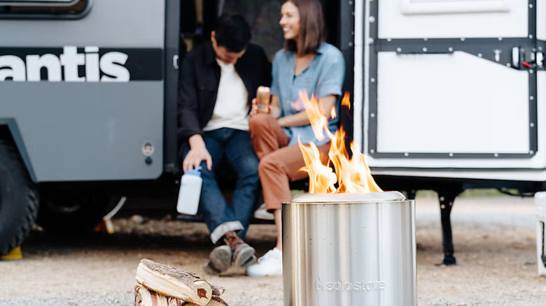 A fire burning in a Solo Stove Ranger with a couple sitting on the steps of their RV