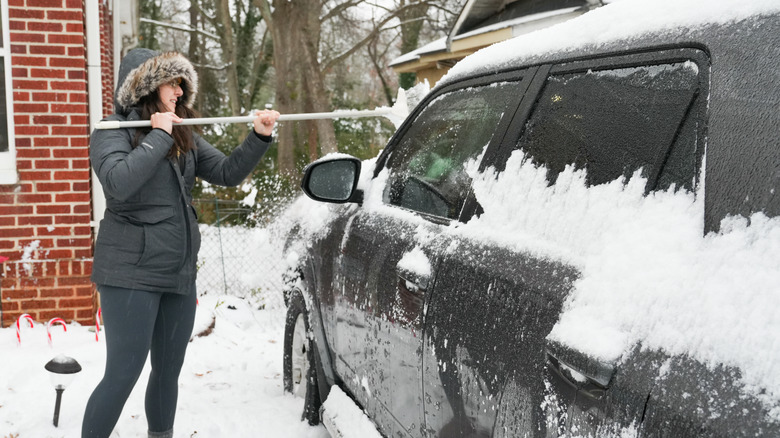 woman uses a broom to clear snow from a vehicle
