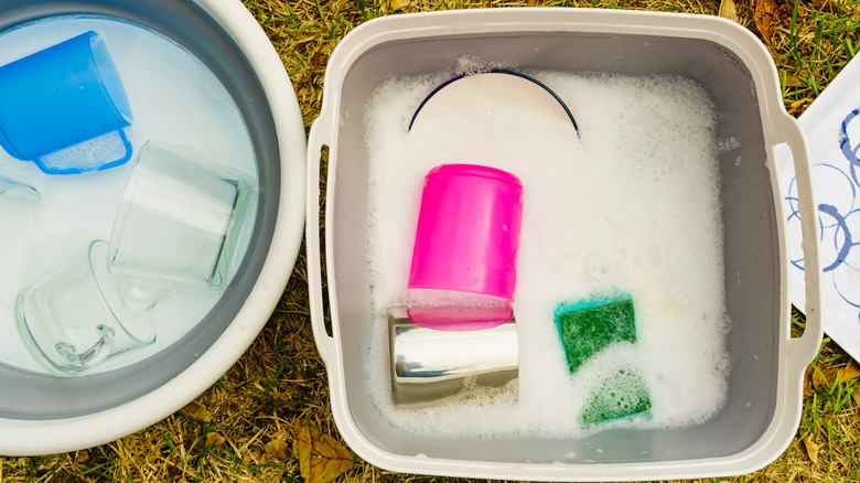 Dirty dishes on the ground in buckets of soapy water