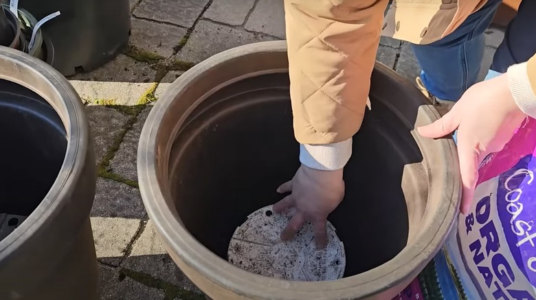 woman putting upside down empty nursery pot in larger planter