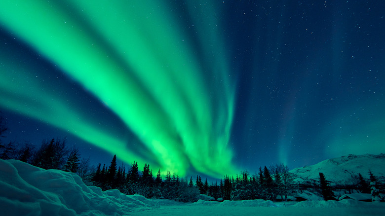 Green northern lights streak over snowy mountains in Alaska
