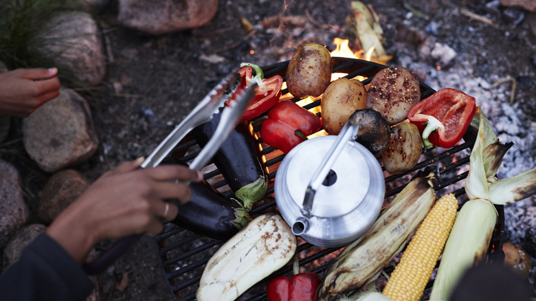 Someone grilling vegetables and heating water on a firepit with tongs