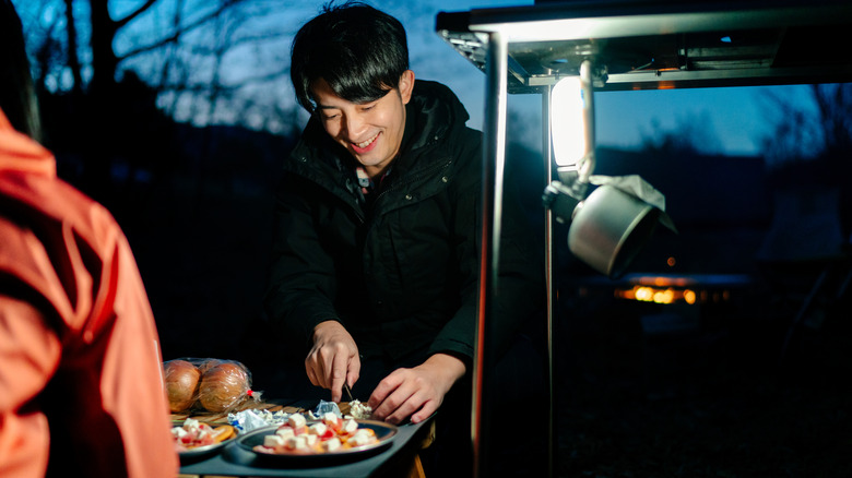 People prepare food while camping at dusk