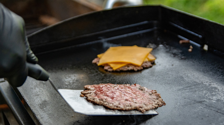 Hand making smash burgers on griddle