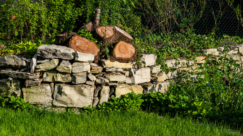 Rock wall with logs on top and lots of greenery on and behind it