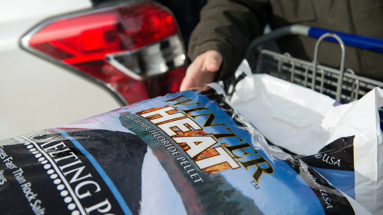 A shopper prepares to load several bags of calcium chloride out of a shopping cart and into their trunk