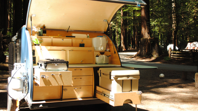 The back of a tiny camper, with a camping stove and cooler, among redwoods