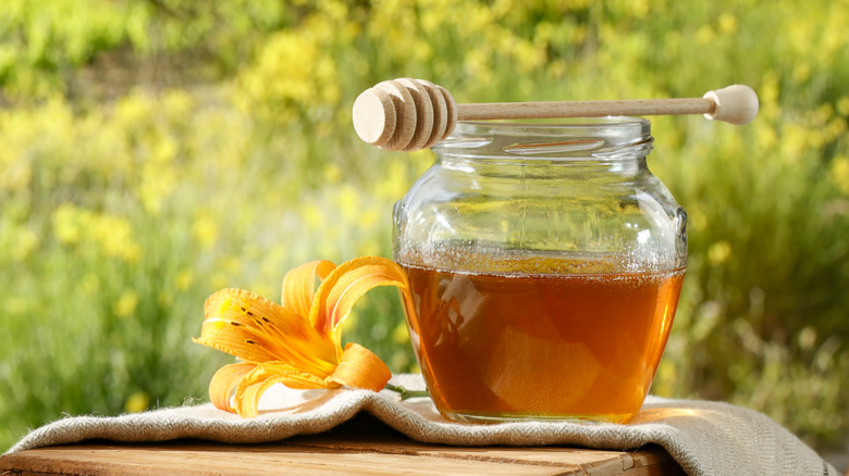Jar of honey with beautiful green grass, hills, and flowers in the background